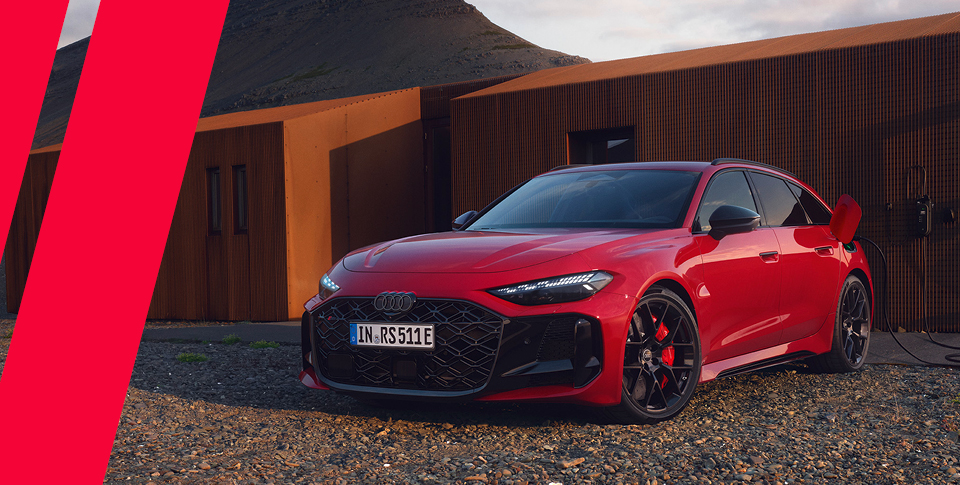 Der neue Audi RS 5 Avant in Rot auf Steinboden vor Holzhaus.