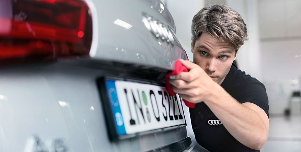 Audi Pflege Service | Junger Mann wischt mit rotem Pflegetuch &uuml;ber Heckklappe eines silbernen Audi